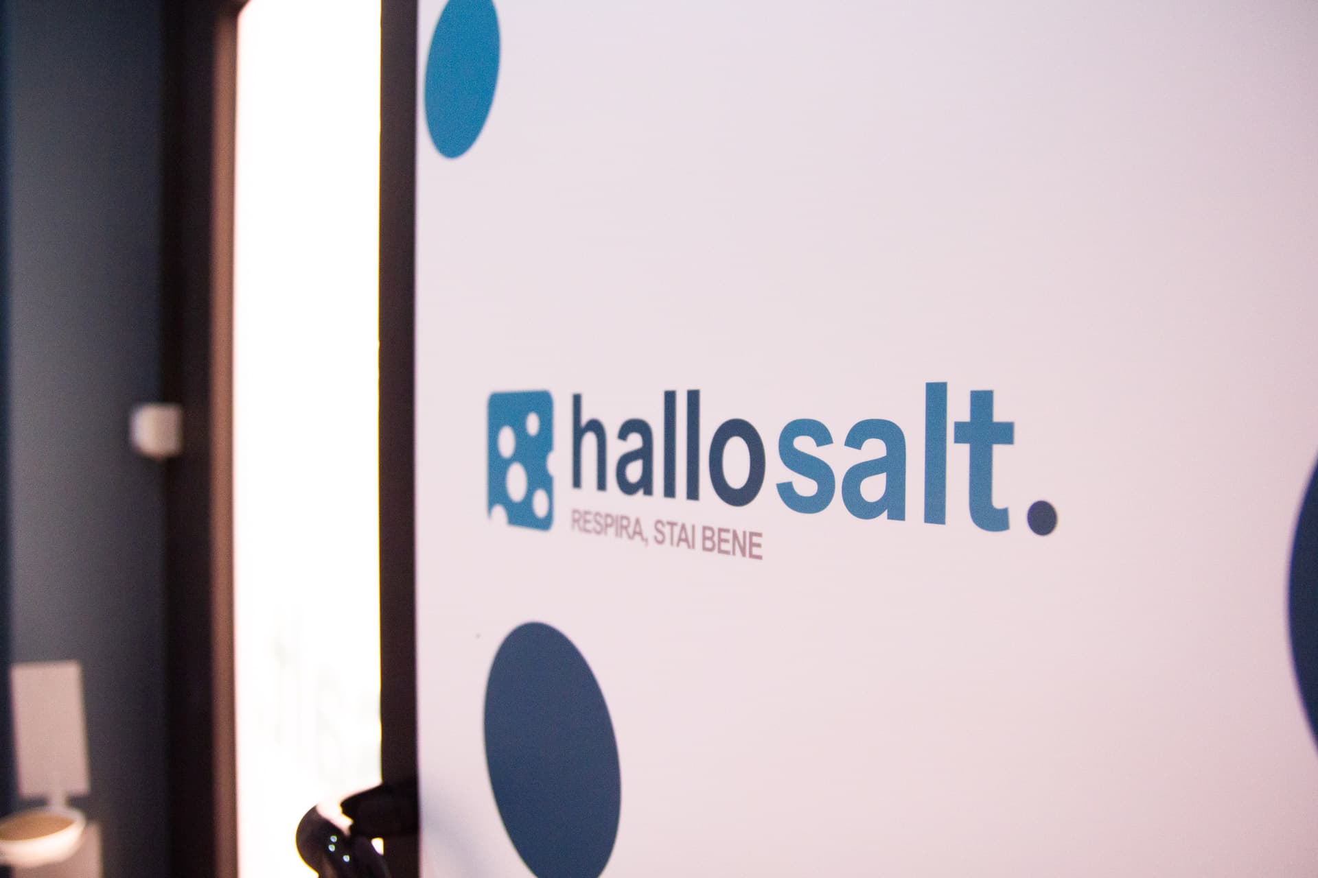Logo hallosalt. e payoff «Respira, stai bene» su vetro bianco a pois blu, all’ingresso del centro.