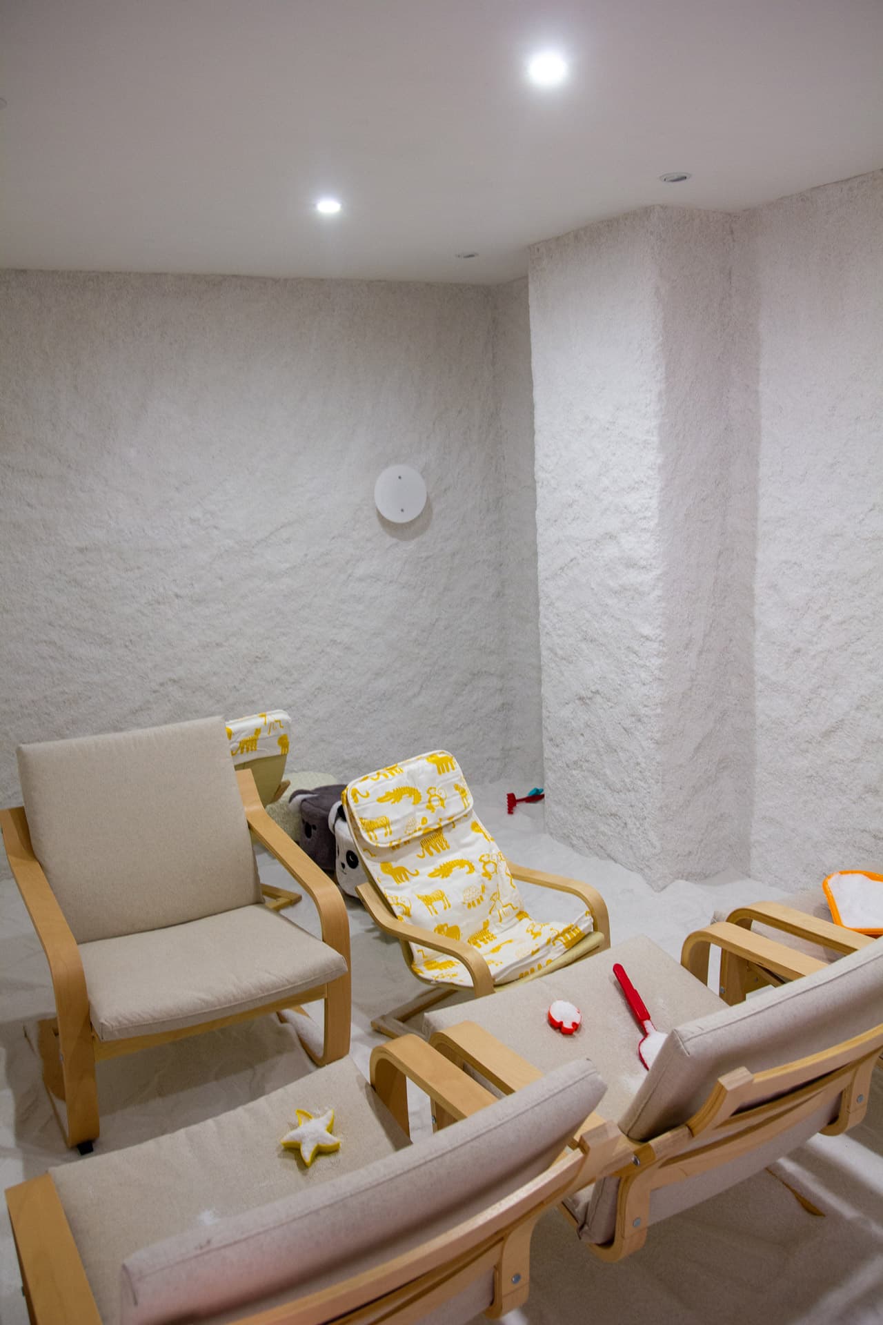 Interno della grotta di sale Hallosalt a Pomezia: pareti e pavimento di sale bianco, poltrone in legno chiaro e giocattoli sparsi sul sale.
